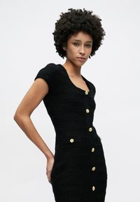 Μαύρο φόρεμα από καρό υφαντό ύφασμα με κοντά μανίκια, λαιμόκοψη σε σχήμα στρογγυλής λαιμής, εφαρμοστή γραμμή, διακοσμημένο με χρυσά κουμπιά και πλαϊνές τσέπες. Λεία υφή.