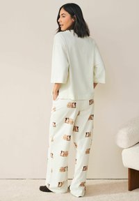 Hellgrünes, oversized Oberteil mit kurzen Ärmeln, kombiniert mit gemusterten, hellen Hosen mit braunen Tiermotiven, aus weichem Stoff.