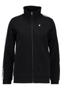 Chaqueta negra con cremallera y cuello alto, stripe blanca de marca a lo largo de las mangas y un pequeño logo en el lado izquierdo del pecho.