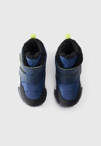 Une paire de bottes d'hiver pour tout-petits de couleur bleue avec des semelles noires, doublure en molleton noir et languettes vertes, vues de dessus sur un fond blanc.