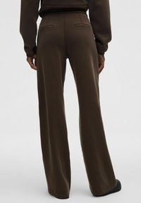 Pantalones de pierna ancha marrones, elaborados con una tela suave, que cuentan con dos bolsillos traseros y una textura lisa con un ajuste ligeramente relajado.