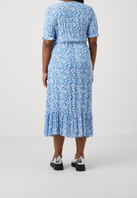 Vestido midi azul con estampado floral, mangas cortas, cintura elástica, dobladillo con volantes y una tela ligera. Combinado con zapatos de plataforma negros brillantes.
