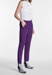 Lila satinbyxor med elastisk midja och sidofickor, kombinerat med en vit ärmlös topp med slående detaljer och ankelstövlar i ormskinnsmönster.