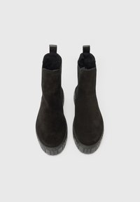 Pár černých semišových kotníkových bot s hrubými gumovými podrážkami a poutky, zobrazených shora na bílém pozadí.