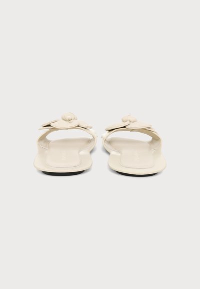 Paire de sandales plates beiges avec bouts carrés et brides nouées, vues de face sur un fond clair uni.