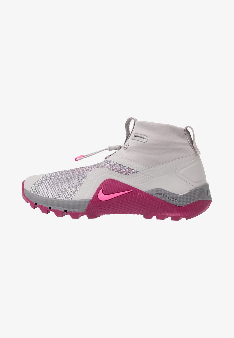 Gros plan d'une chaussure de sport Nike Metcon grise et rose avec une tige en mesh, un col montant au niveau de la cheville, et une semelle extérieure texturée pour une bonne adhérence.