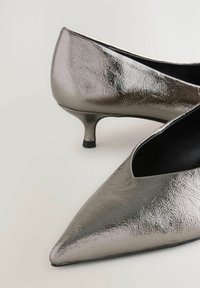 Zapatos de tacón alto metálicos plateados con punta afilada, que cuentan con una superficie texturizada y un tacón estrecho y curvado para mayor elegancia.