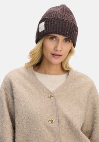 Dziergana czapka w głębokim fioletowym kolorze z kolorowymi akcentami. Miękka, prążkowana tekstura. Towarzyszy jej kremowy kardigan z okrągłymi guzikami.