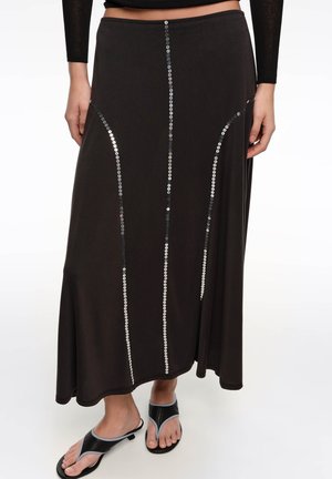 Falda larga negra con rayas verticales de lentejuelas plateadas, combinada con top negro de manga larga y sandalias negras de tacón abierto.