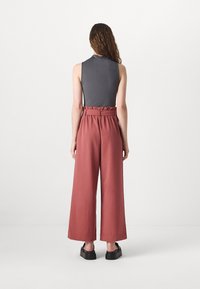 High-waisted, wide-leg pants in soft, textured rust fabric, featuring a belted waist and a flowing silhouette. Styled with a fitted gray top.