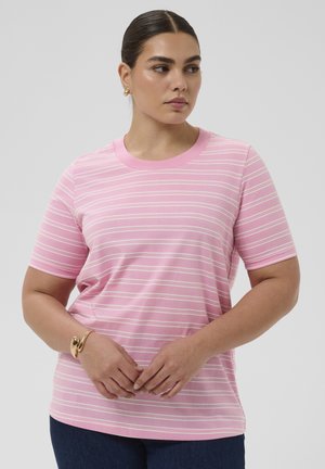 Žena u ružičasto-bijeloj prugastoj majici kratkih rukava, zlatnoj narukvici i naušnicama, s rukama složenim ispred sebe, gleda udesno.