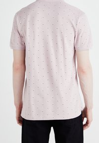 Světle růžová polo tričko s texturovanou tkaninou, krátkými rukávy a opakovaným malým námořnickým tečkovaným vzorem.