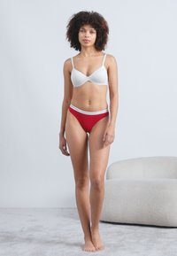 Λευκό σουτιέν με επένδυση και κόκκινα εσώρουχα με ψηλή μέση που διαθέτουν λευκή λωρίδα με λογότυπο. Λείο ύφασμα, εφαρμοστή σχεδίαση και αόρατες άκρες για άνεση.