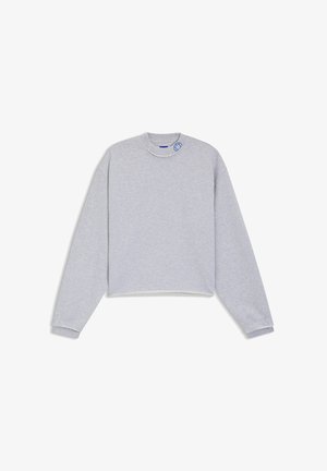 Sudadera gris claro recortada con mangas largas, puños acanalados, dobladillo sin rematar y pequeño detalle bordado en azul cerca del cuello.