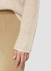 Helle pink gestrickte Pullover mit gerippter Textur, mit einem sanften, flauschigen Finish und einem weißen, fransigen Saum. Beigefarbene, eng anliegende Hose darunter.