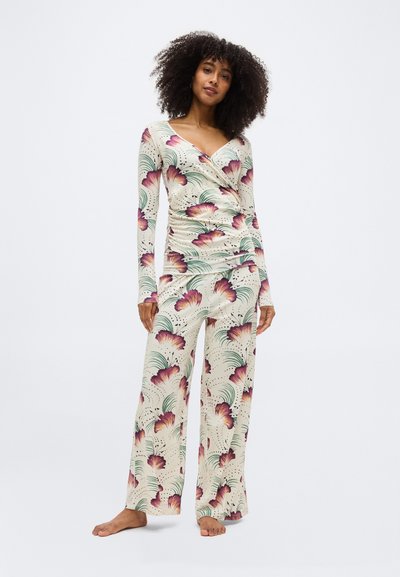 Femme debout pieds nus portant un ensemble assorti composé d'un haut à manches longues crème et d'un pantalon large imprimé floral violet et vert.