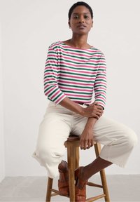 Gestreepte lange mouwen top met rode, groene en witte lijnen; zachte katoenstof; boot halslijn; gecombineerd met crèmekleurige cropped broek en bruine schoenen.