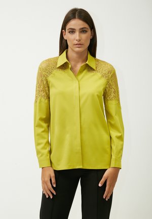 Limoengroene blouse met lange mouwen, een kraag en kantaccenten op de schouders, gemaakt van een glanzende, lichte stof.