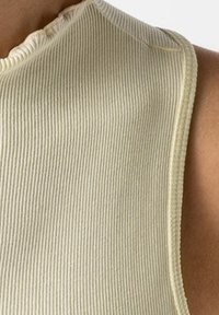 Ribbad ärmlös topp i ljusbeige med rund halsringning och textilstruktur, med en mjuk, fransig kant längs kragen.