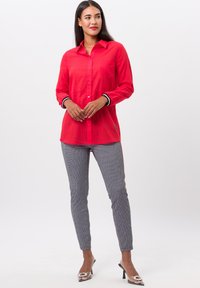 Rode button-up blouse met een zak, gecombineerd met grijze gestreepte broek met een slanke pasvorm. Transparante hakken maken de outfit compleet.