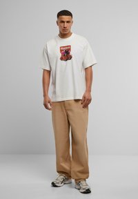 Camiseta de algodón blanca con un colorido estampado gráfico que dice "Mercado" y un coche rojo. Combinada con pantalones de pierna ancha de color beige claro y zapatillas.