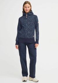 Marinblå sweatshirt med hög krage, blommönster i blått och vitt, tre stora knappar, ribbade ärmslut och en logotyp på ärmen.