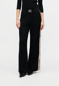 Μαύρο παντελόνι με φαρδύ πόδι και απαλό υλικό, διακοσμημένο με πλαϊνή ριγωτή λεπτομέρεια, χρυσά κουμπιά και λογότυπο στη μέση.