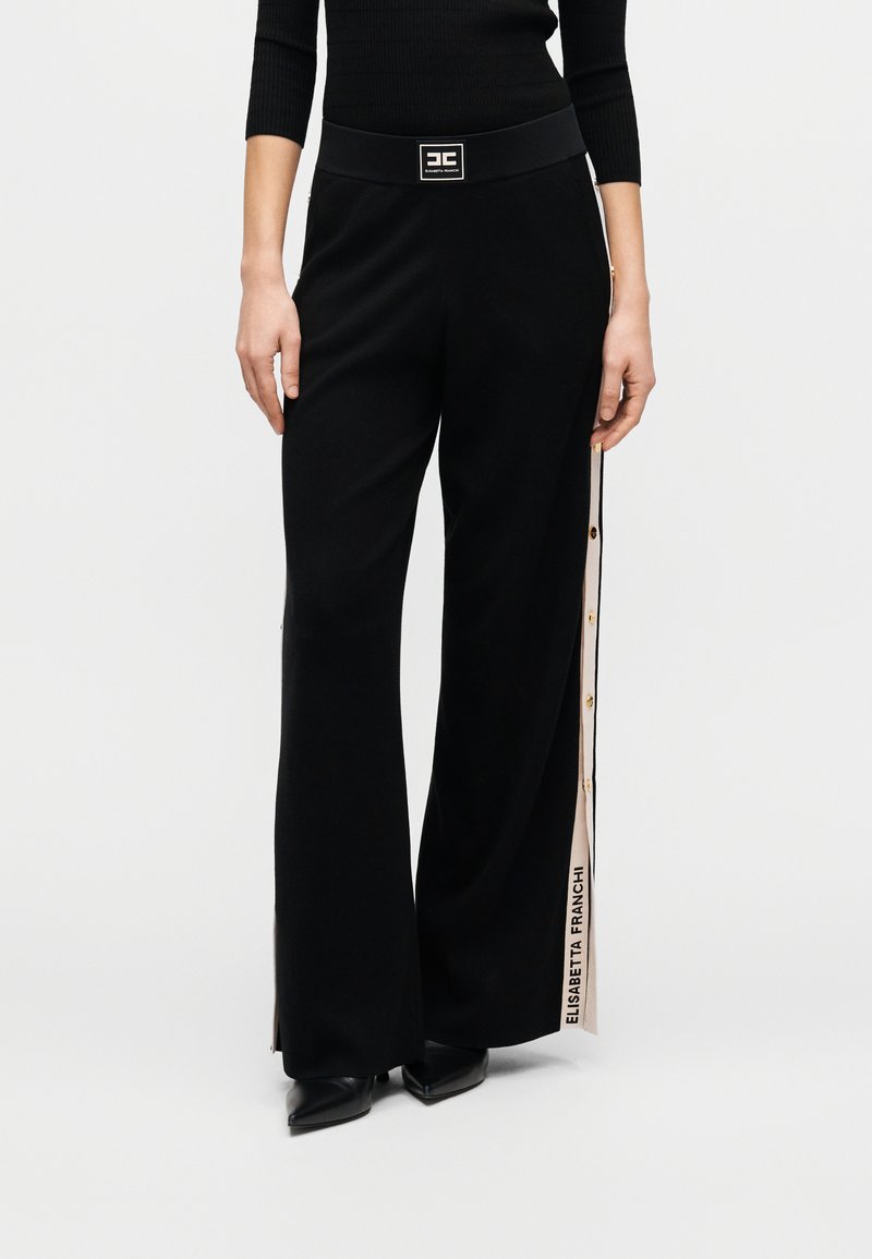 Μαύρο παντελόνι με φαρδύ πόδι και απαλό υλικό, διακοσμημένο με πλαϊνή ριγωτή λεπτομέρεια, χρυσά κουμπιά και λογότυπο στη μέση.