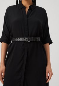 Abito nero a camicia con bottoni davanti, maniche corte e una cintura in pelle nera abbinata con occhielli in metallo e una fibbia classica.