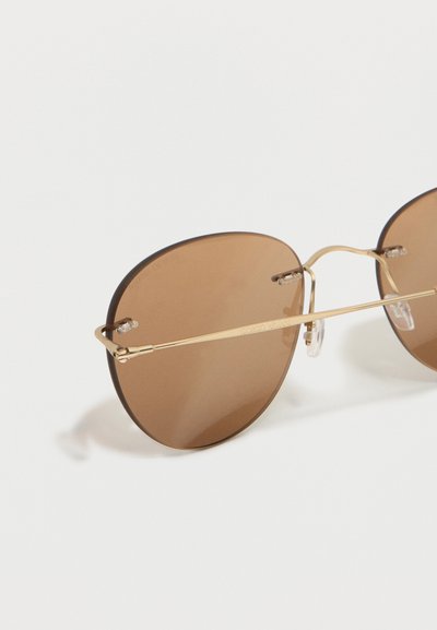Στρογγυλά καφέ φιμέ γυαλιά ηλίου με λεπτό χρυσό μεταλλικό σκελετό και πιονιά μύτης σε λευκό φόντο.