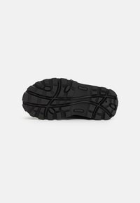 Black rubber shoe sole with deep tread, featuring multi-directional patterns and textured surface for grip and stability.