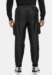 Svarta cargobyxor med elastisk midja, sidofickor och smalnade avslut. Tillverkade av glänsande, mjukt material med en avslappnad passform.