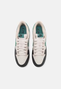 Nikes tenisky s krémovým koženým svrškem, zelenými akcenty a černou gumovou podrážkou. Mají kulaté tkaničky a perforovaný špičkový díl pro ventilaci.