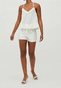 Top bianco senza maniche con design a occhiello e orlo arricciato, abbinato a pantaloni corti bianchi. Entrambi sono leggeri con una texture morbida.
