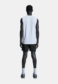Weißes ärmelloses Sportshirt, schwarze Shorts, graue Turnschuhe, sichtbare Stoffstruktur und kontrastierende weiße Socken. Ein minimalistisches Design von hinten.