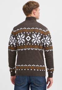 Maglione marrone lavorato a maglia con colletto alto; presenta motivi di fiocchi di neve bianchi e marroni sul petto e sulle spalle. Polsini e orlo a coste.