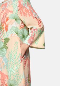 Kleid mit Blumenmuster aus weichem Pfirsichstoff, das grüne und rote botanische Designs zeigt; lockere Ärmel und seitliche Taschen erhöhen die Funktionalität.