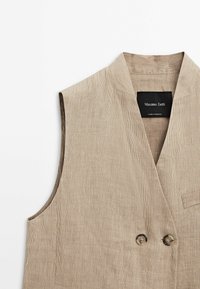 Beige kordflöjtsväst med v-ringning, utan ärmar, två bruna knappar och en enkel bröstficka, märkt "Massimo Dutti."