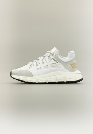 Zapatilla Versace en blanco y gris con diseño de cordones, suela gruesa con patrón de llave griega y detalle del logo dorado en el talón.