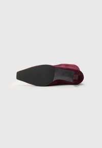 Burgunderfarget semsket ankelstøvel med spiss tå og glatt svart gummisåle, med en liten hæl og minimalistiske designelementer.