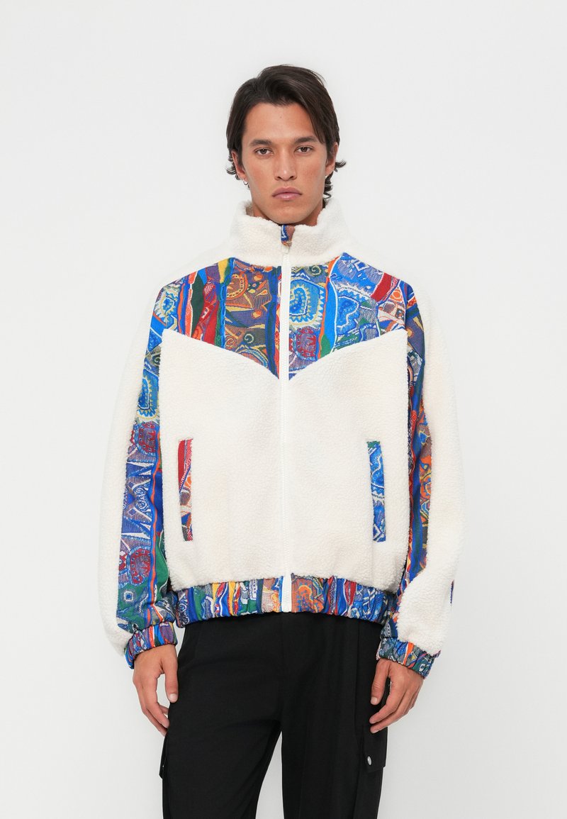 Fleece jacket with a high collar, featuring a white body and colorful patterned sleeves. Zippered front and side pockets.