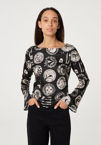 Zwarte lange mouwen top met een ronde halslijn, voorzien van een wit patroon van cirkelvormige motieven en ontwerpen. Zachte, gladde stof met een aansluitende pasvorm.