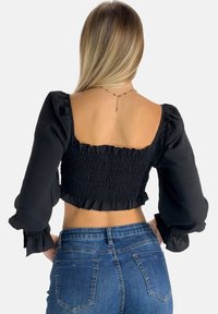 Sort smocket crop top med puffede ærmer, forskudt kant og firkantet rygdesign. Parret med blå denim jeans.