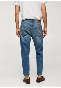Pantalones de mezclilla azul con un corte ajustado, que cuentan con dos bolsillos traseros y un parche de cuero en la cintura. La tela tiene una apariencia ligeramente desgastada.