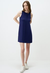 Ärmelloses, navyfarbenes Kleid mit geradem Schnitt, glatter Textur und minimalen Nahtdetails. Tragen mit weißen Sneakers für einen lässigen Look.