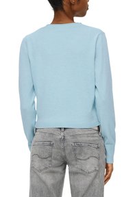 Jasnoniebieski sweter z dzianiny z długimi rękawami, ściągaczowym wykończeniem i okrągłym dekoltem, w zestawie z szarymi dżinsami z detalami przeszycia kieszeni z tyłu.