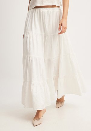 Jupe maxi blanche à volants en tissu léger avec une texture froncée, dotée d'une taille élastique et d'une silhouette fluide.