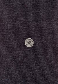 Tessuto lavorato a maglia grigio scuro con un piccolo logo metallico circolare al centro con il testo "Burlington the Original."