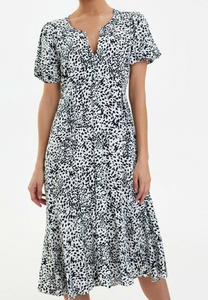 Mujer con un vestido midi blanco con un estampado de puntos negros irregulares, mangas cortas abullonadas y escote en V.