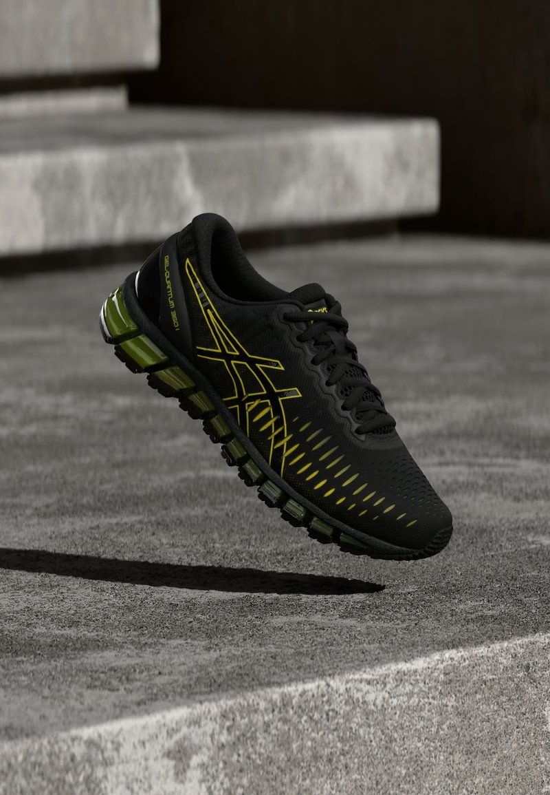 Chaussure de sport noire et verte avec des accents jaunes flottant au-dessus de marches en béton, mettant en valeur la semelle rembourrée et le design élégant.